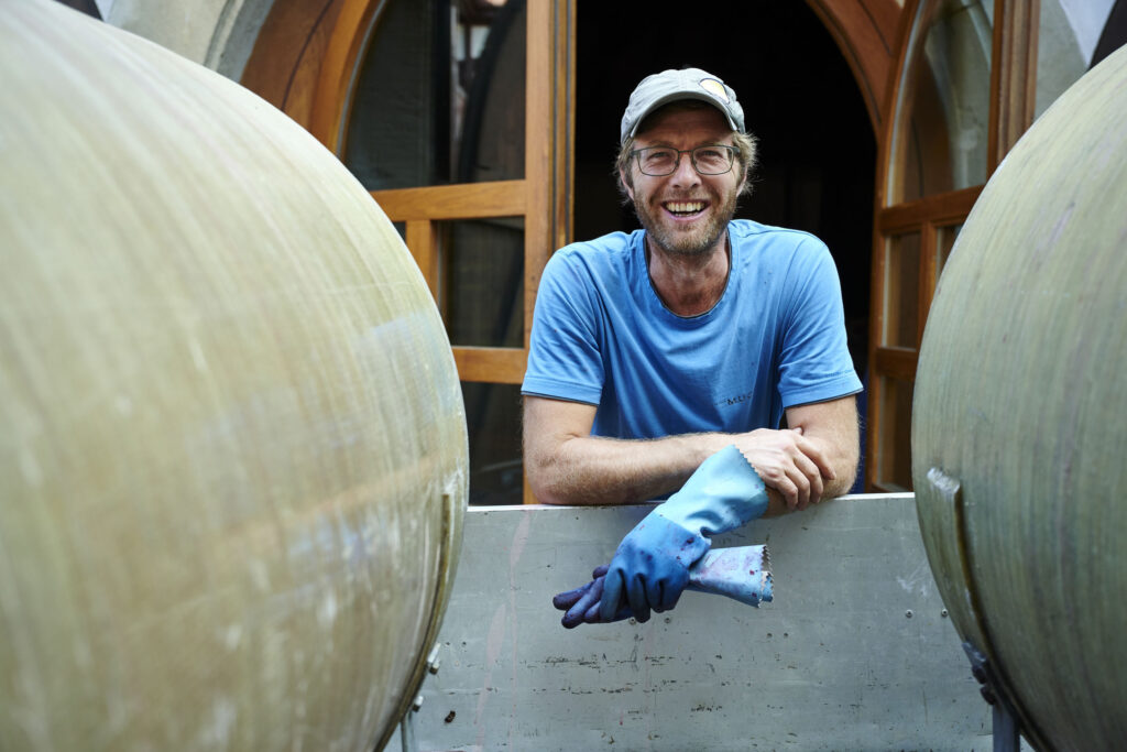 Ein Mann mit blauem T-Shirt, Brille und Kappe lächelt in die Kamera.