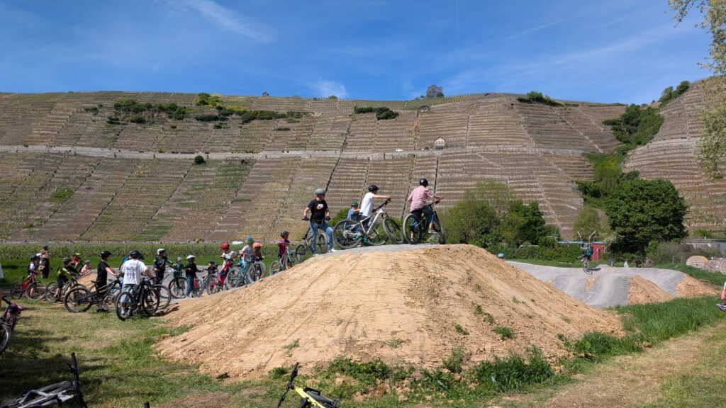 Mehrere Radfahrer mit Helmen stehen am Starthügel an. Im Hintergrund sind die terrassierten Weinsteillagen zu sehen.